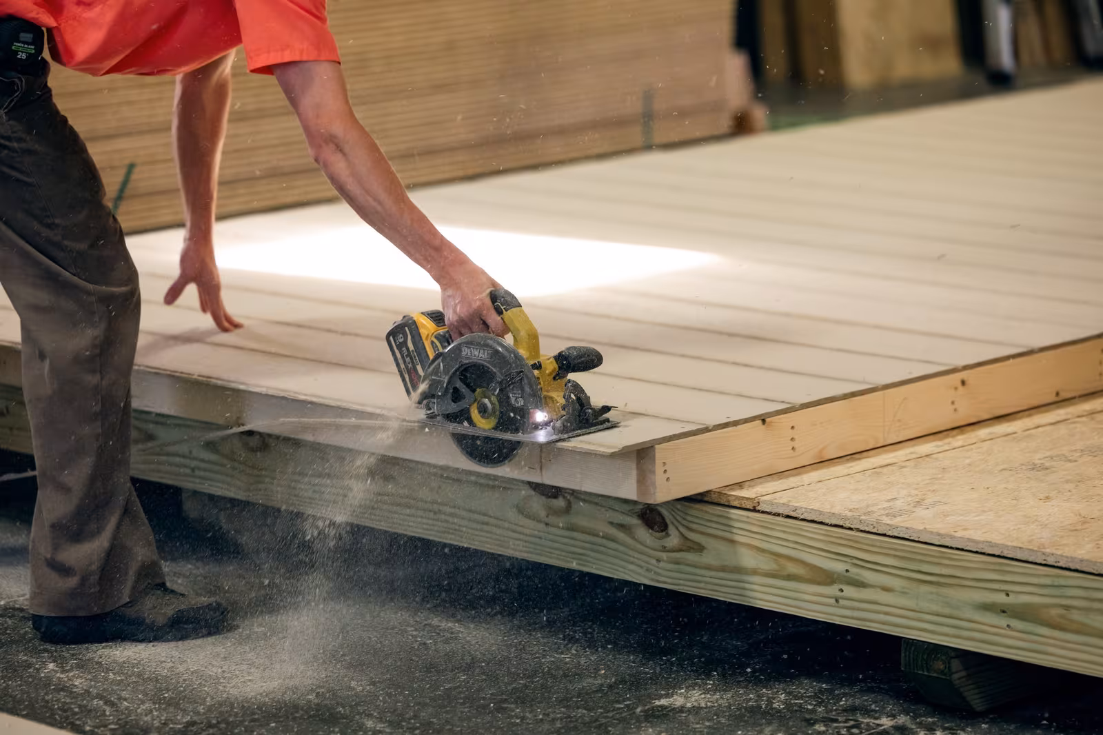 An Amish builder cutting a shed floor panel with a circular saw, sawdust in the air
