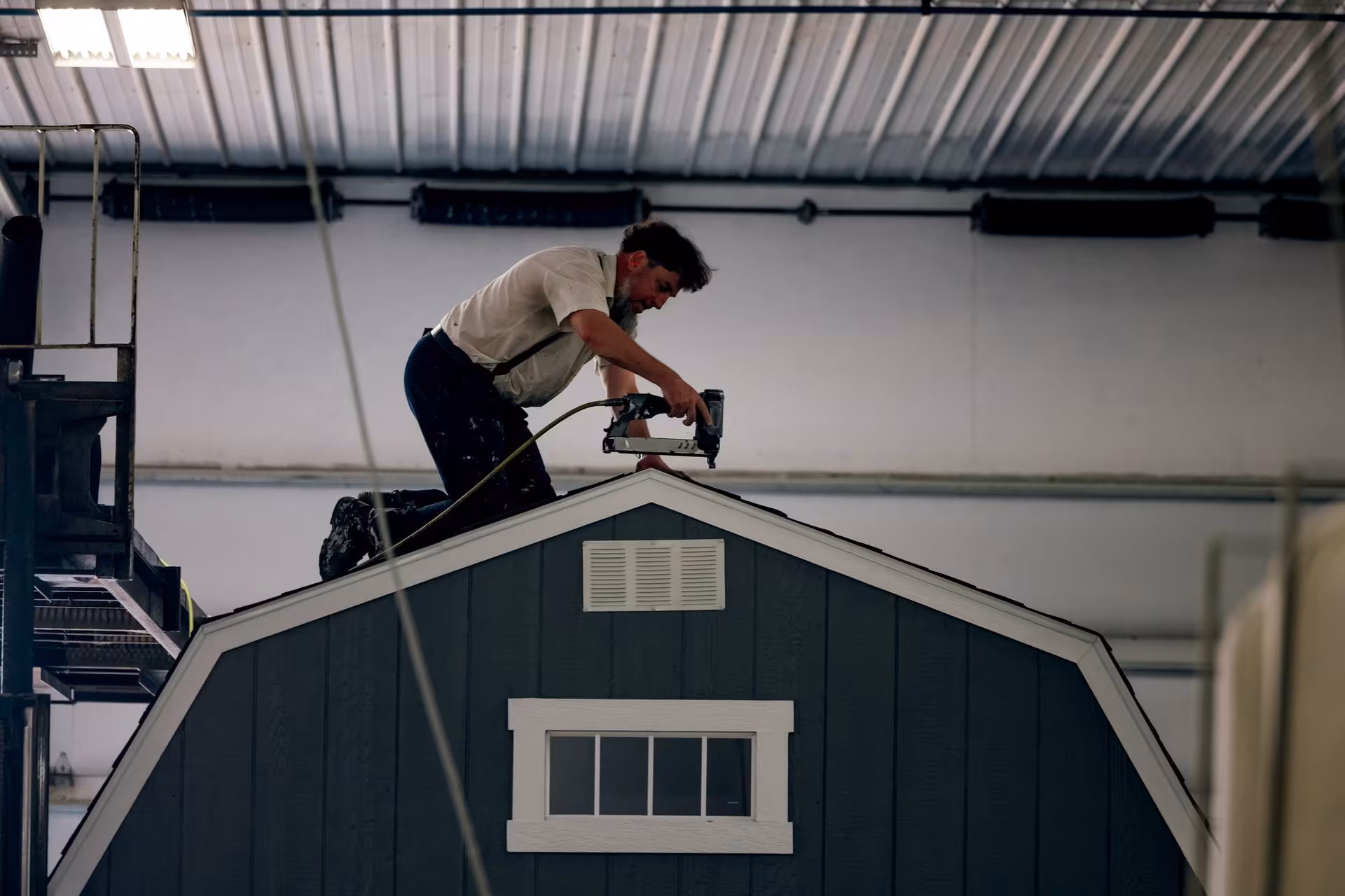 An Amish builder nailing the gambrel roof of a barn-style shed in the workshop