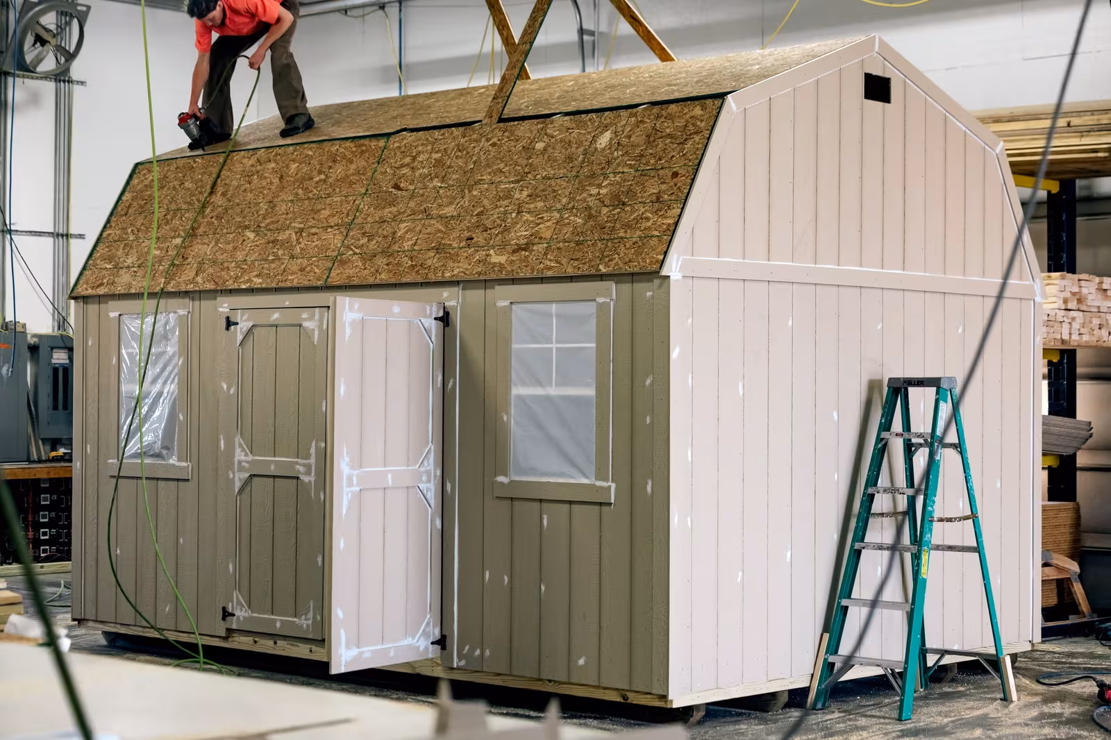 An Amish builder finishing the roof of a barn-style shed in the workshop