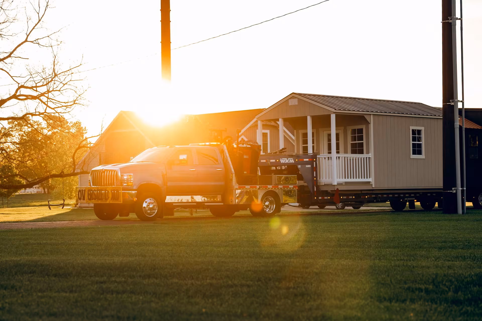 An Amish Outdoor Buildings truck delivering a porch cabin at sunrise